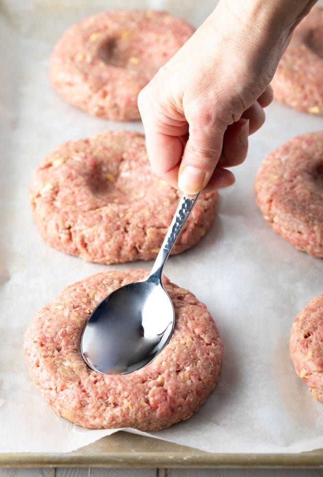 Hand using a spoon to make a small dent in the hamburger patties before cooking. 