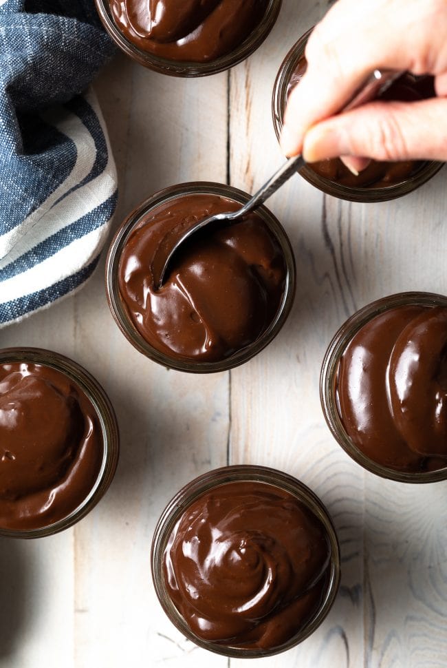 Hand dipping a spoon into a smooth homemade chocolate pudding in a jar. 