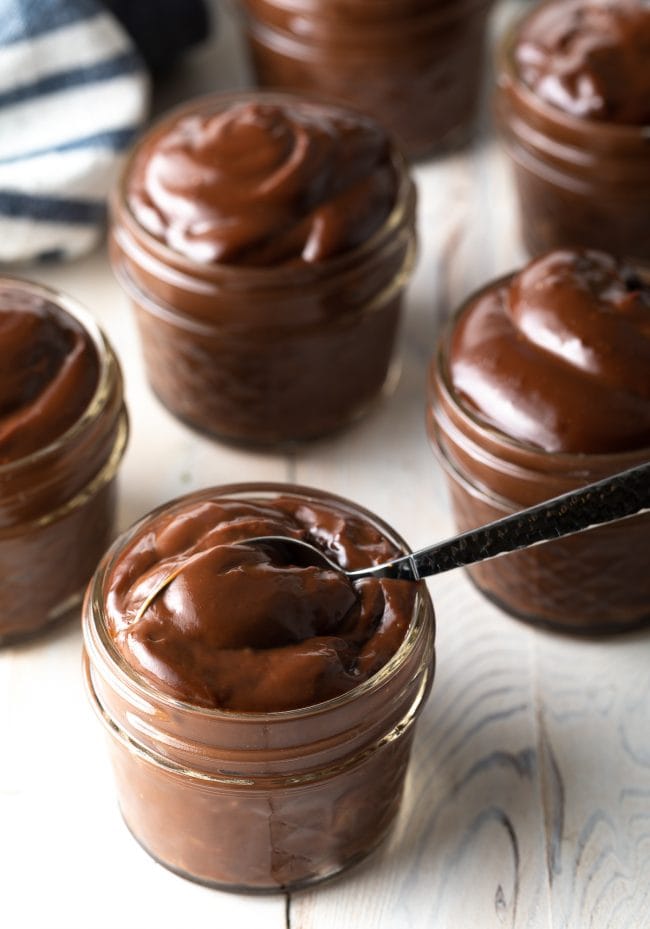 Spoon in a jar of pudding with more jars of chocolate pudding behind it. 