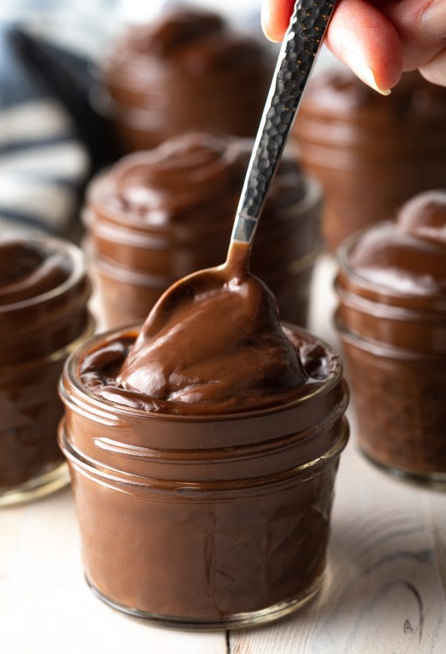 Hand holding a spoon scooping a bite of chocolate pudding recipe from a small jar. 