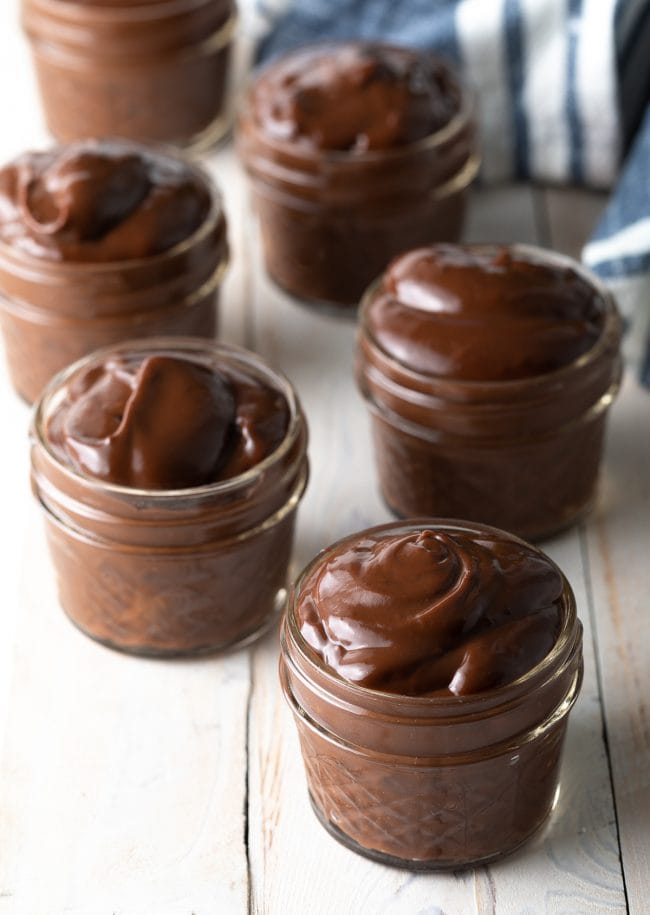 Little jars lined up and filled with chocolate pudding recipe. 