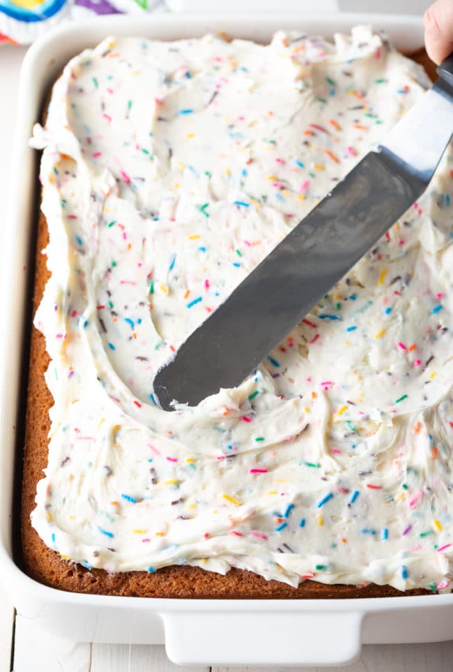 Offset spatula being used to spread funfetti icing on the sheet cake. 