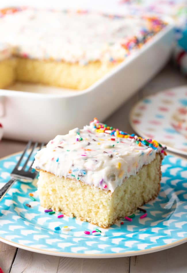 Slice of vanilla cake with funfetti frosting served on a blue plate. 