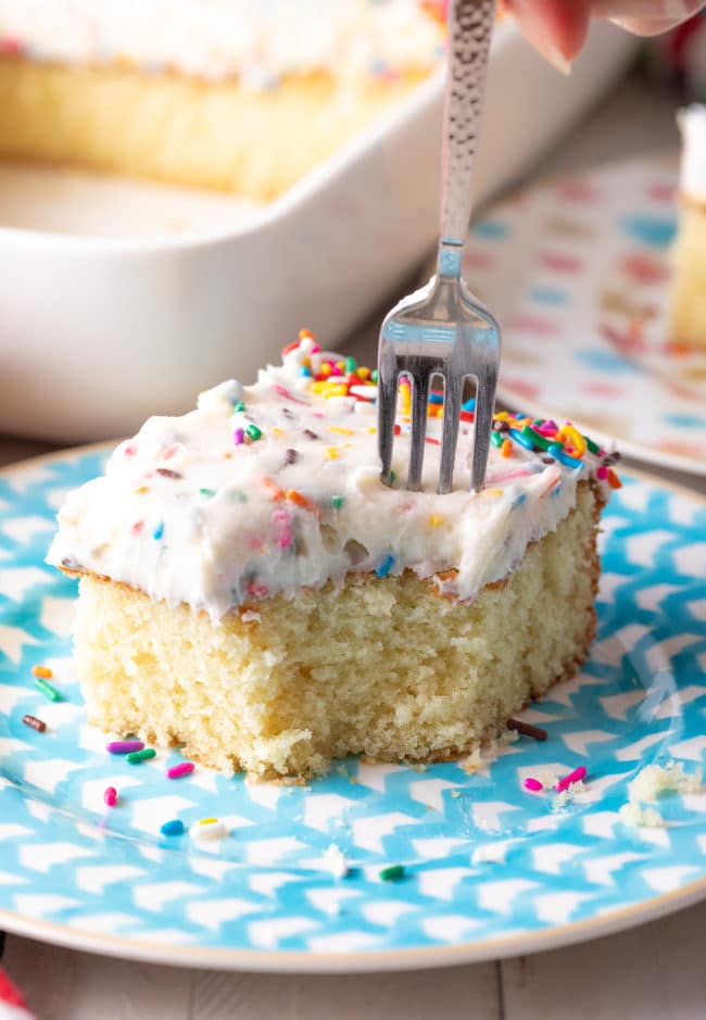 Vanilla cake on a plate with a fork taking a piece. 