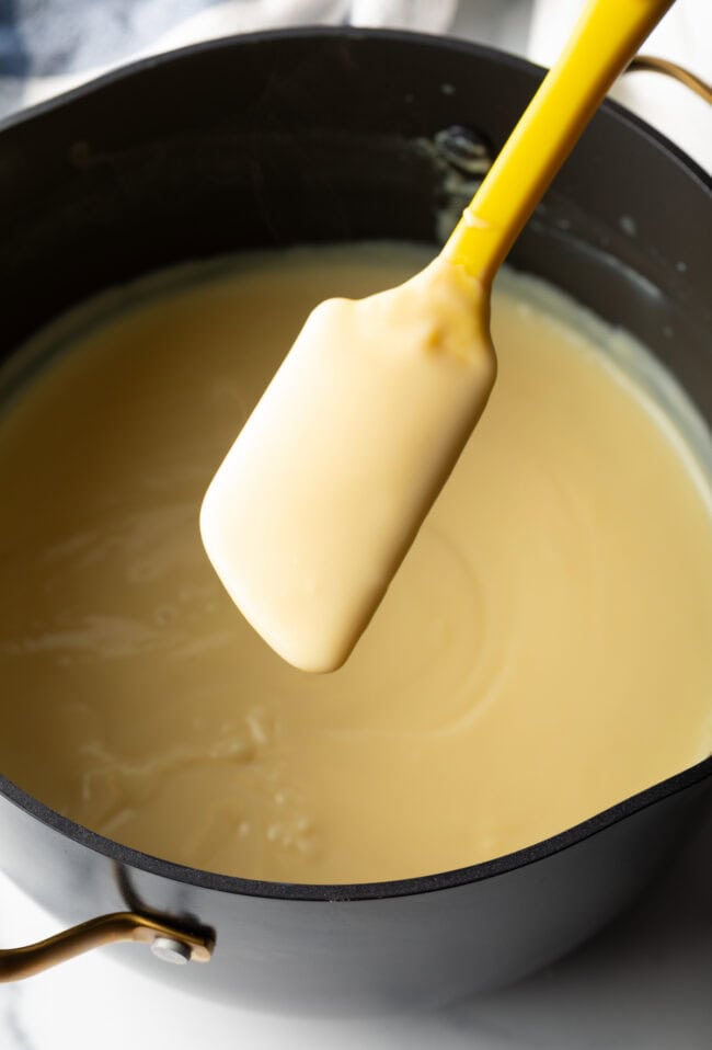 Spatula coated with vanilla pudding recipe, held over pot of pudding.