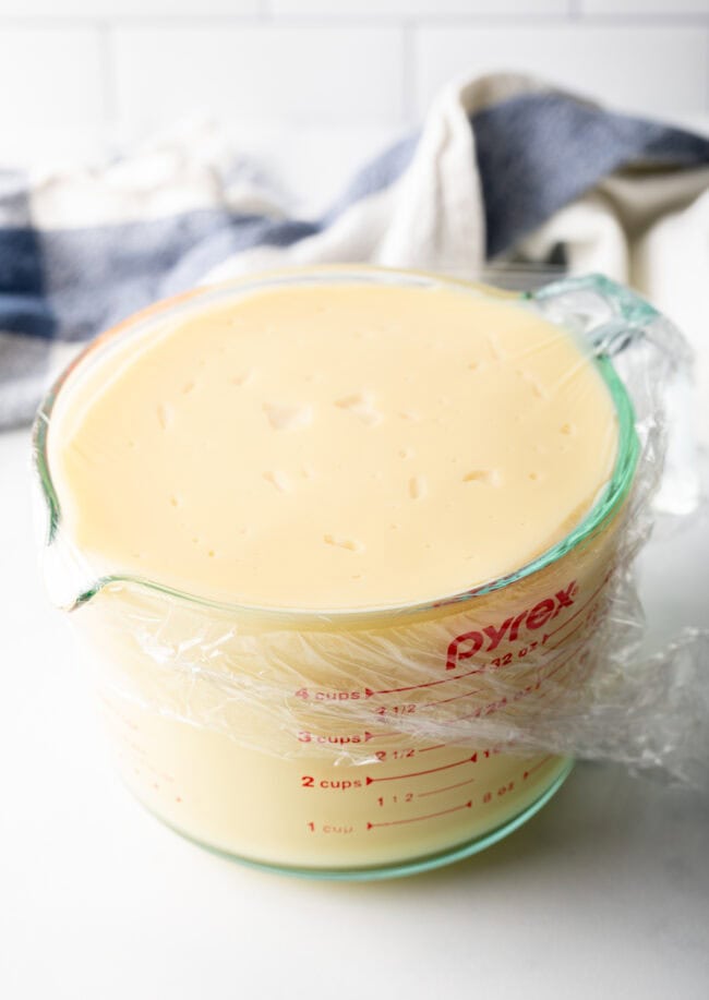 Large glass measuring cup filled with pudding, piece of plastic cling film covers the cup.