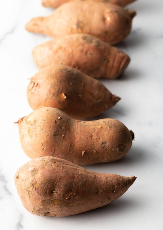 Row of 4 raw potatoes on a white board.