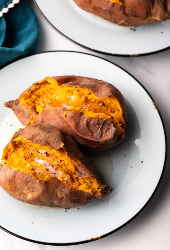 2 cooked potatoes on a white plate, each is opened on top with a pat of butter inside.