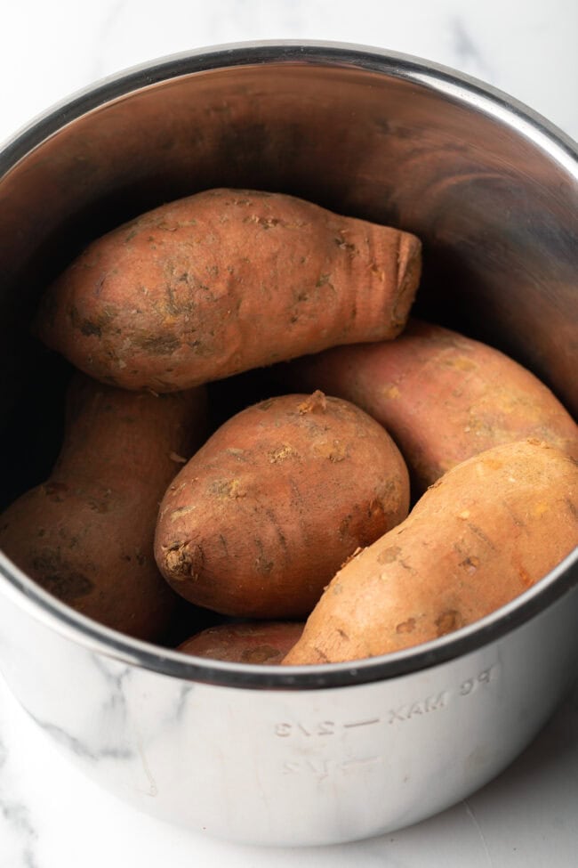 Metal pot with 6 raw sweet potatoes inside.