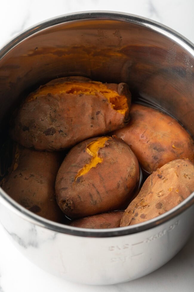 Metal pot with 6 cooked sweet potatoes inside.