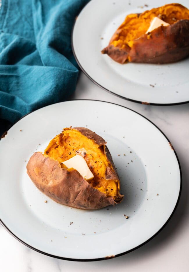 1 cooked sweet potato on a white plate, opened on top with a pat of butter inside.