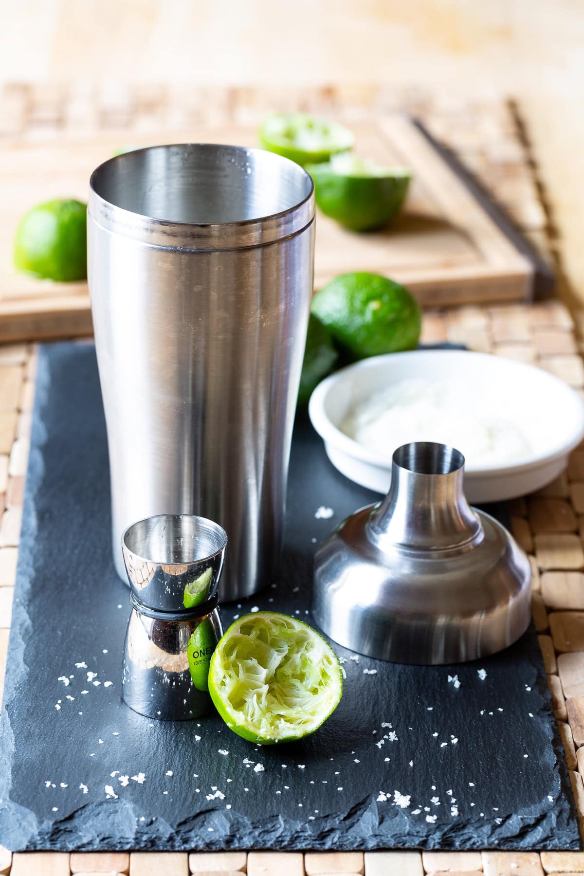 Cocktail shaker next to a jigger and limes. 