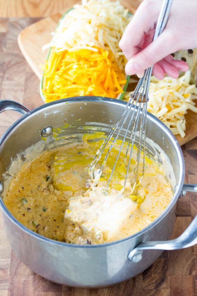 Hand mixing queso ingredients in pot with a whisk. 