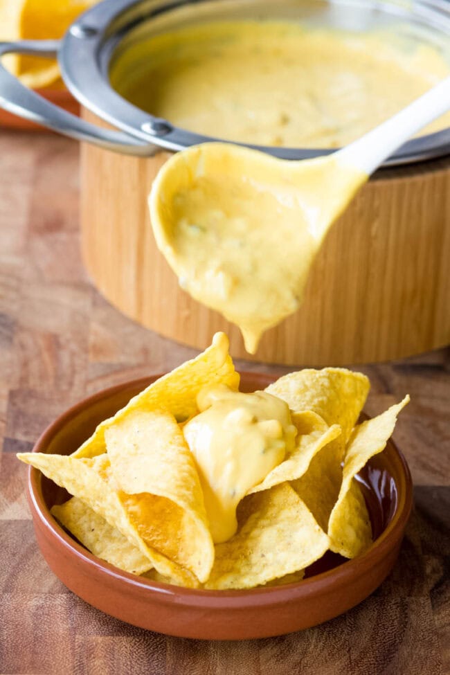 Cheese sauce dripping over tortilla chips with a ladle. 