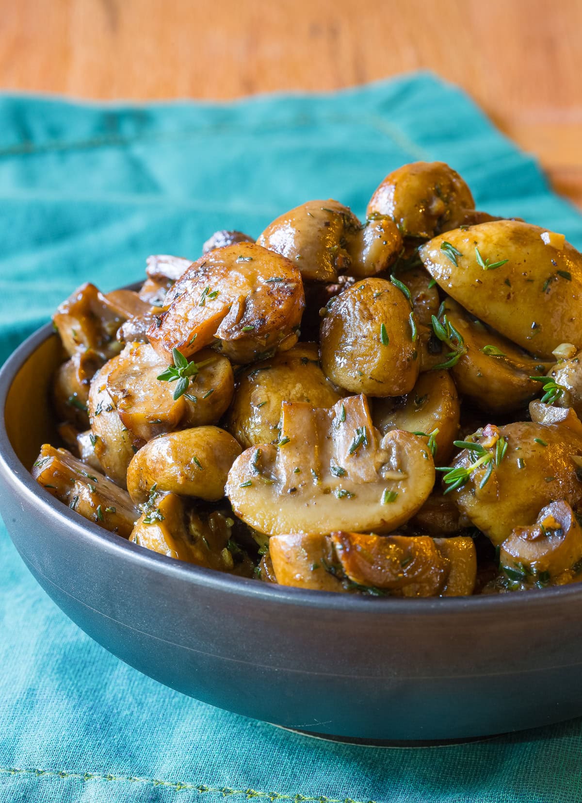 Serving bowl filled with sautéed mushrooms with thyme sprinkled on top. 
