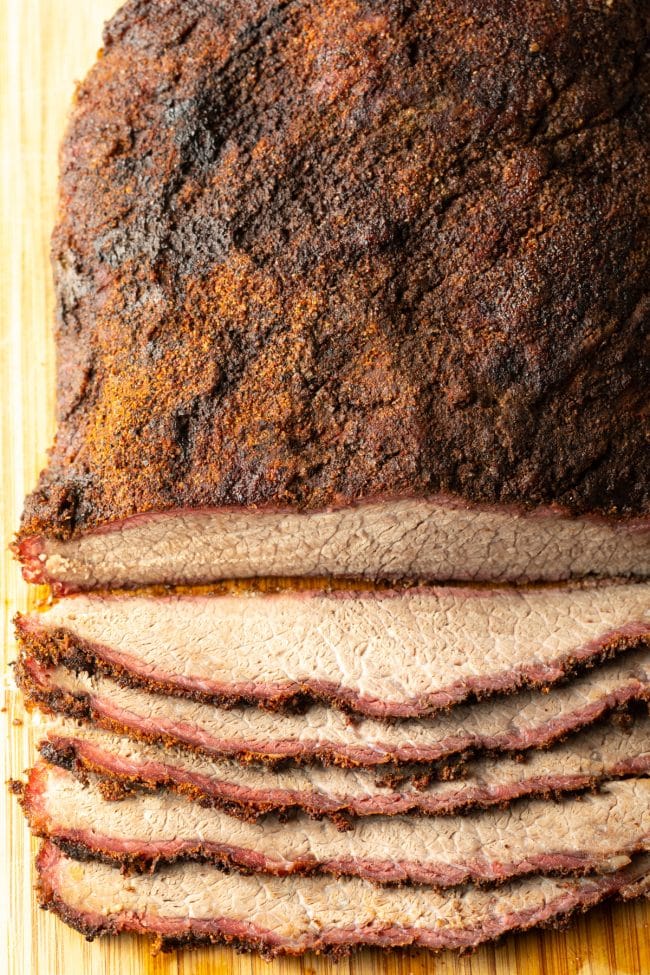 smoked beef brisket on a wooden cutting board with some pieces sliced off of the edge. 