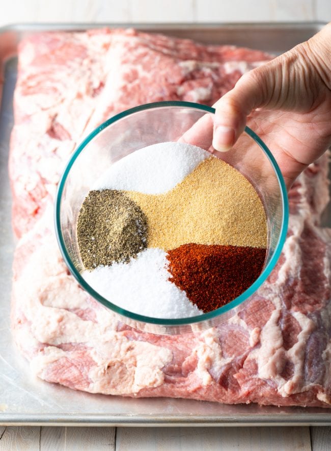 brisket brine spice rub in a glass bowl, being held above a raw beef brisket. 