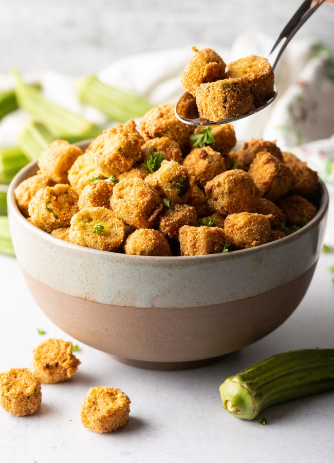 Spoon adding pieces of southern fried okra to a bowl.