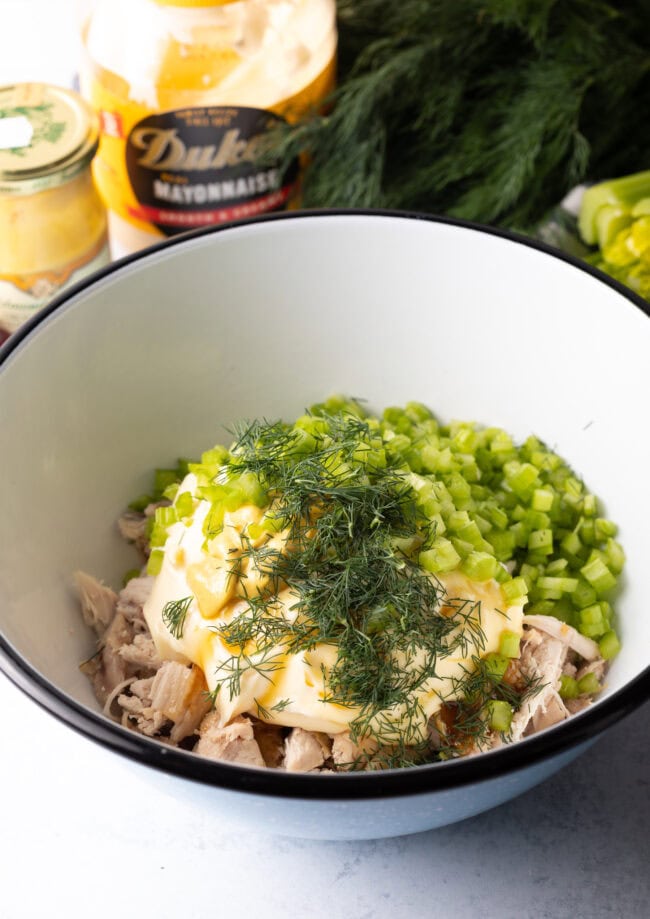 White bowl with shredded poultry, mayo, celery, and fresh dill.