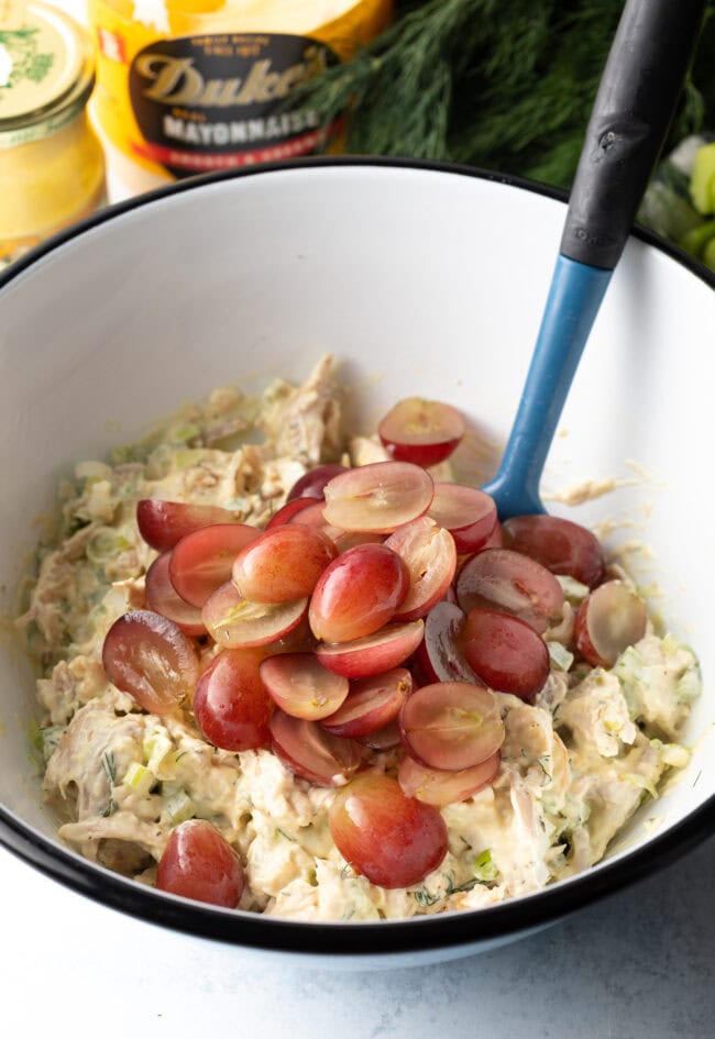 Adding halved grapes to the bowl.