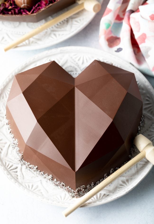 chocolate shell breakable heart on a white plate with a small hammer