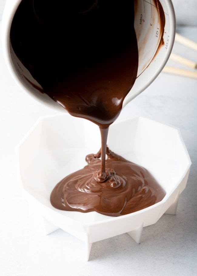 pouring melted chocolate from white measuring cup into the white silicone heart shell mold