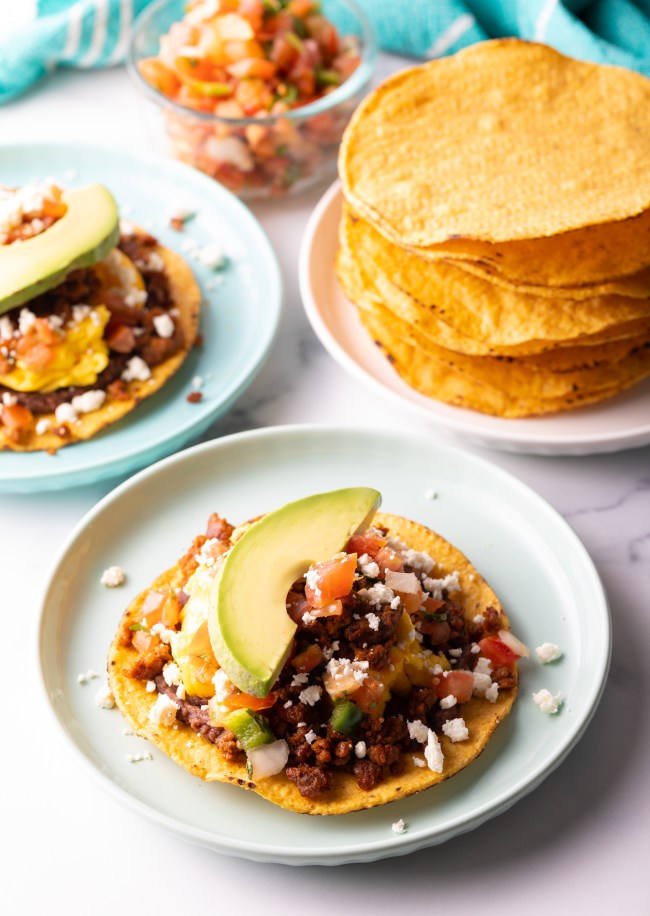 Breakfast tostado loaded with ingredients and slice of avocado.