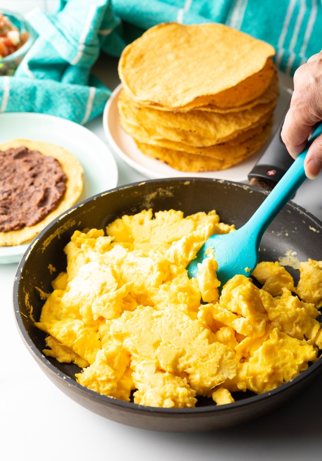 Scrambled eggs in a skillet, stirred by a blue spatula.