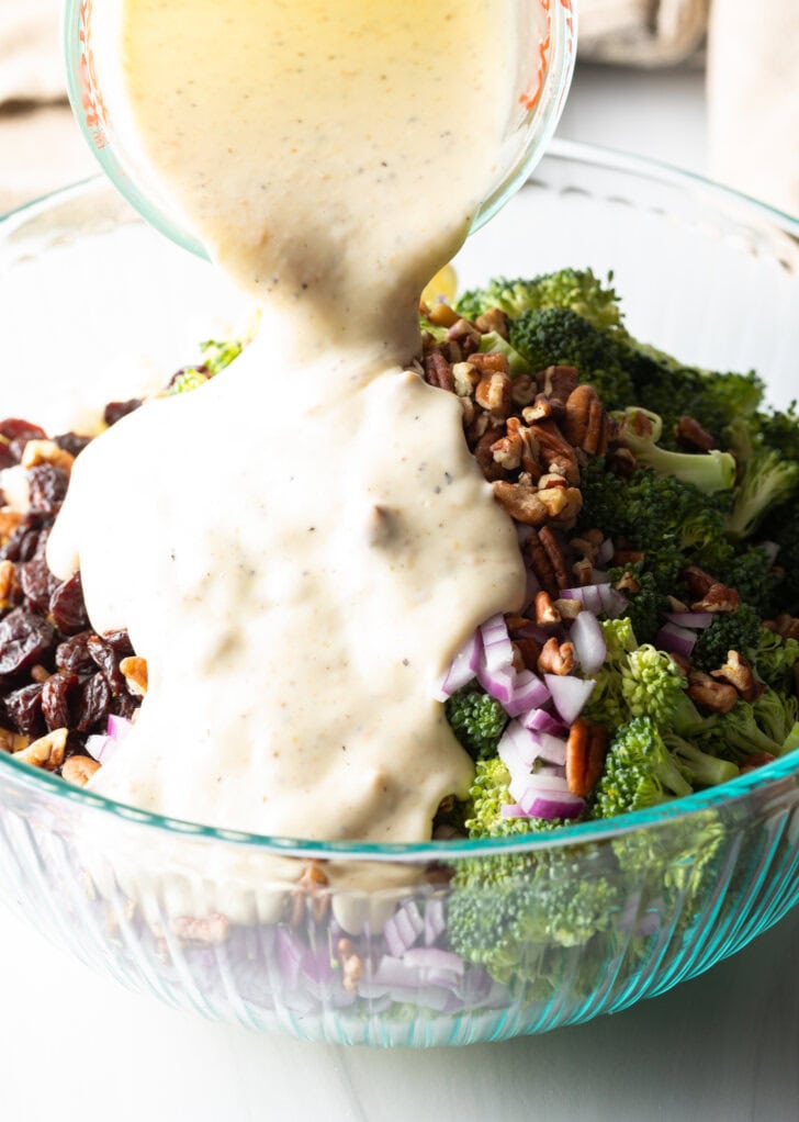 Adding creamy mayo dressing from a glass measuring cup onto the salad ingredients in a large glass bowl.