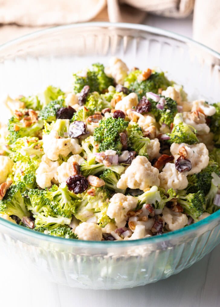 Bowl of cauliflower and broccoli salad tossed with pecans, red onions, and cranberries.