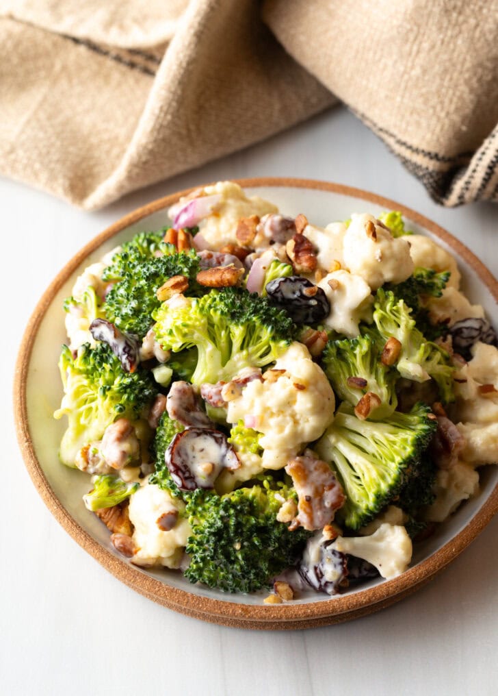 Bowl of cauliflower and broccoli salad tossed with pecans, red onions, and cranberries.