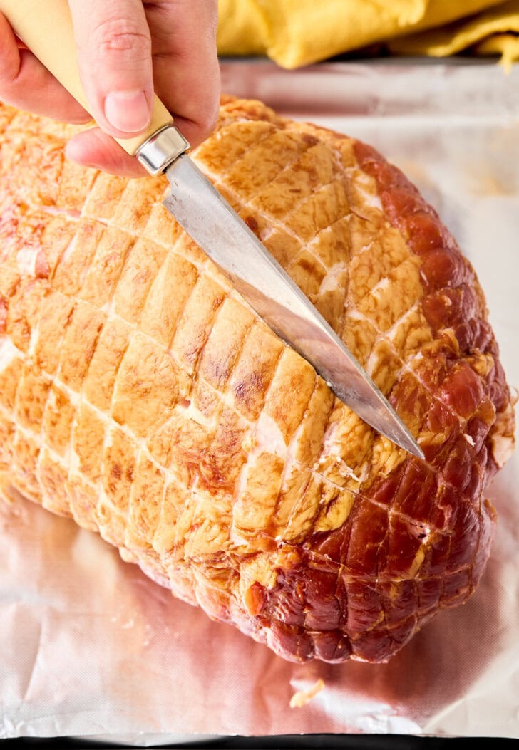 Hand holding a sharp knife to score the top of the unbaked ham. 