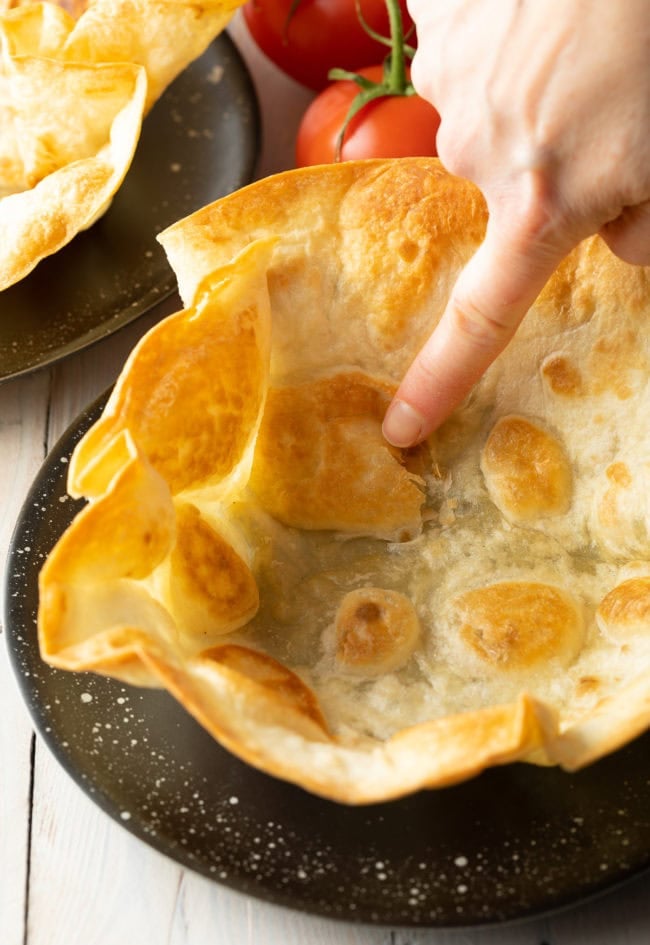 Taco bowl shell on a plate with a hand poking to show how crispy it is. 