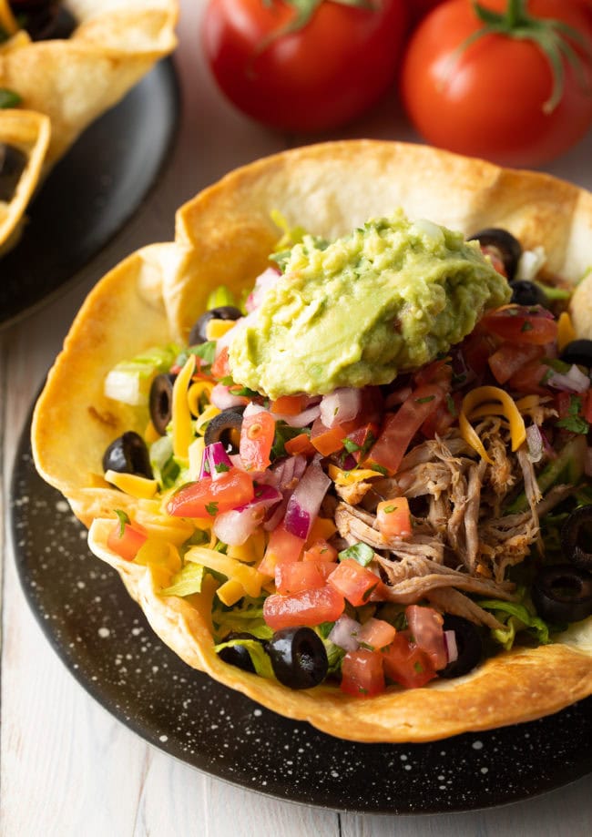 Taco salad in a shell served on a black plate. 