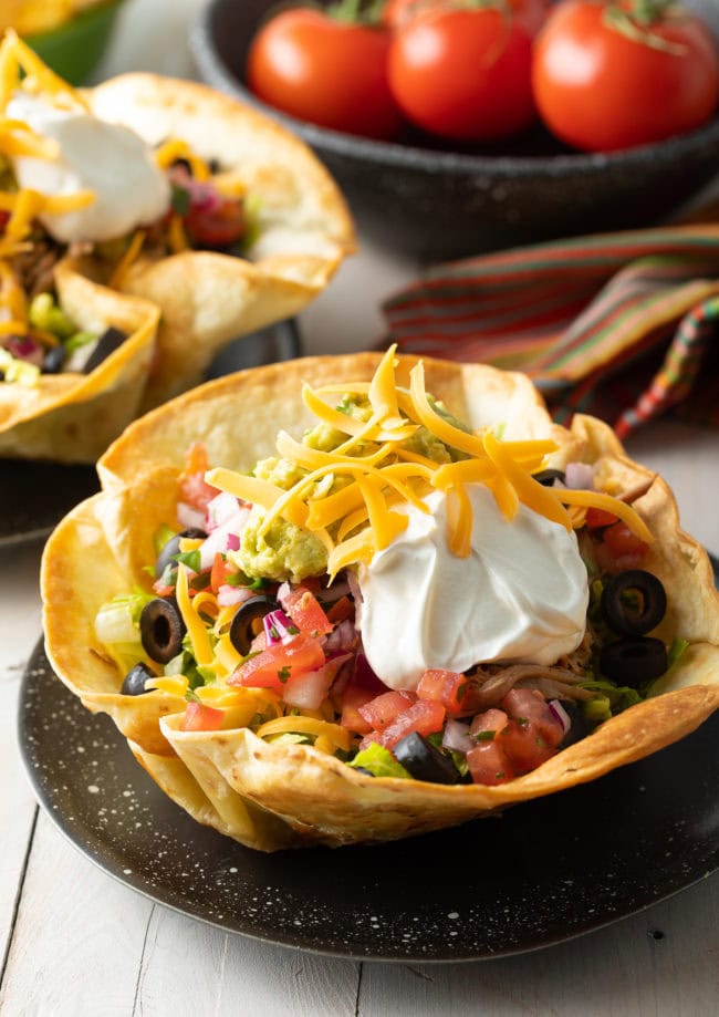 Tortilla Bowls filled with taco salad and served on black plates. 