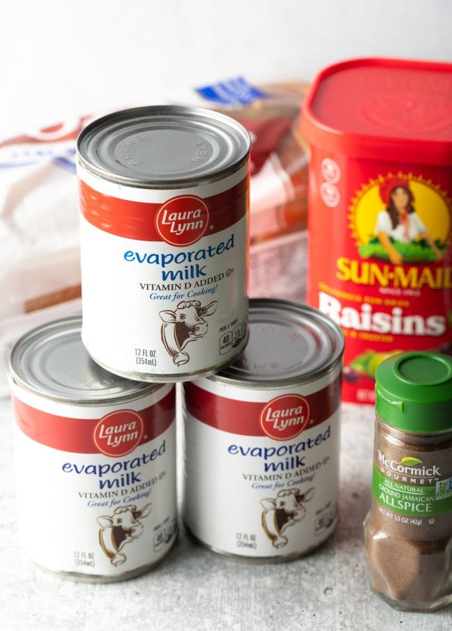 Evaporated milk, container of raisins, and bottle of allspices on a kitchen counter. 