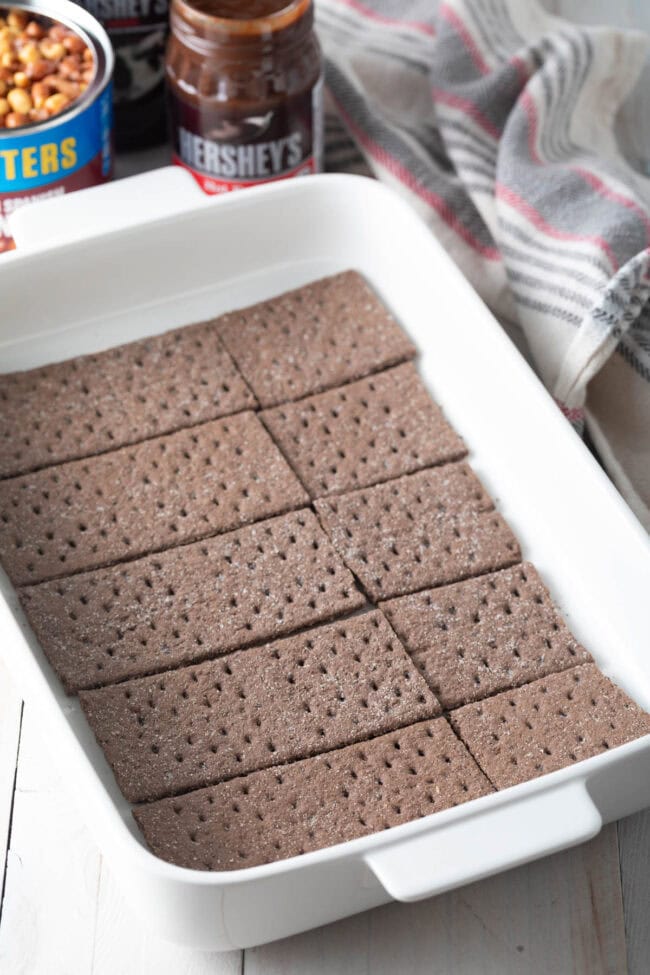 First layer of chocolate graham crackers in a white baking dish. 