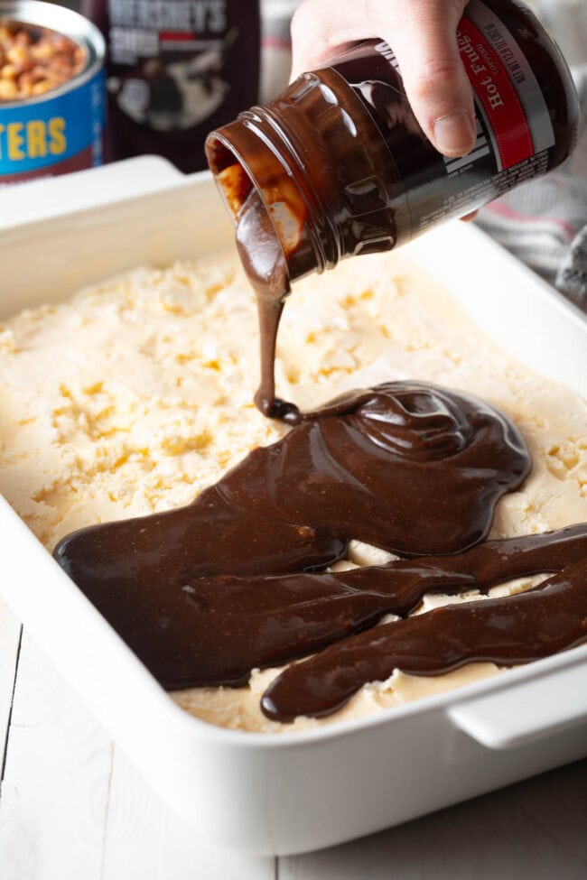 Hand pouring layer of hot fudge layer into the ice cream cake. 