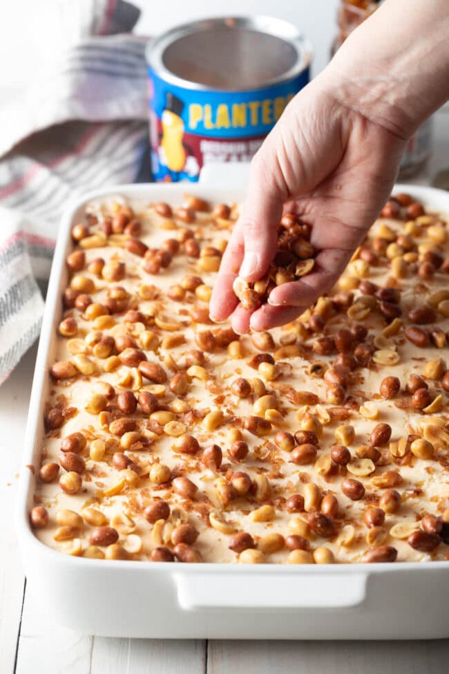 Hand sprinkling a layer of peanuts on top of the cake. 