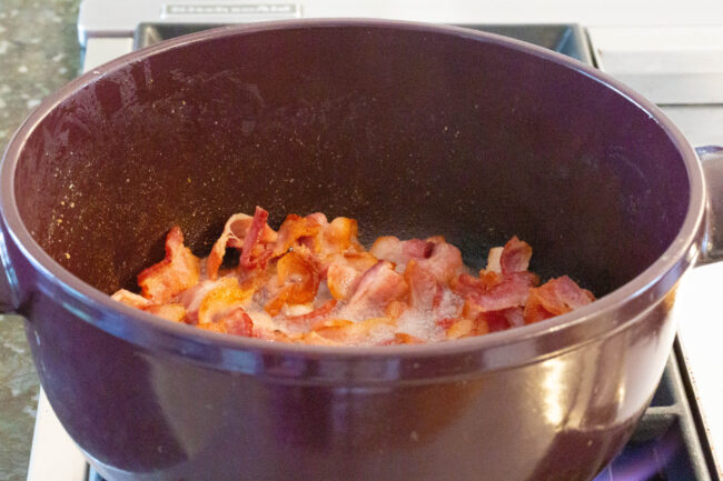 Bacon cooking in a large pot on the stove. 