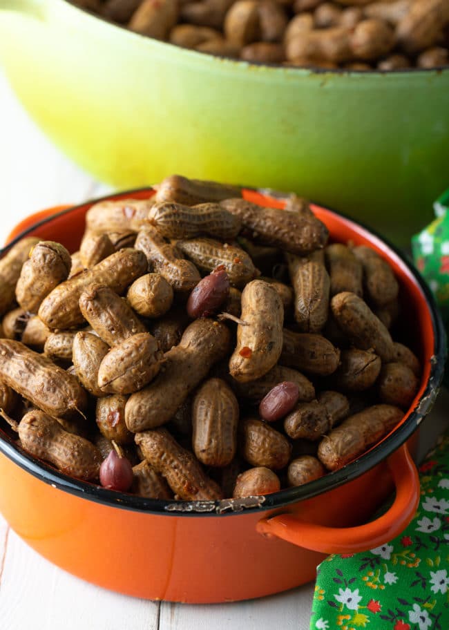 Boiled peanuts in an orange pot next to a larger pot with more peanuts in it. 