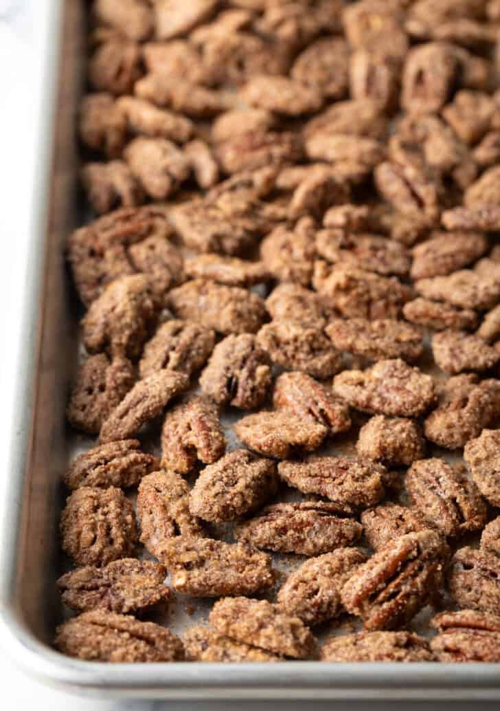 Dried pecans coated in cinnamon and sugar spread out on a baking sheet.