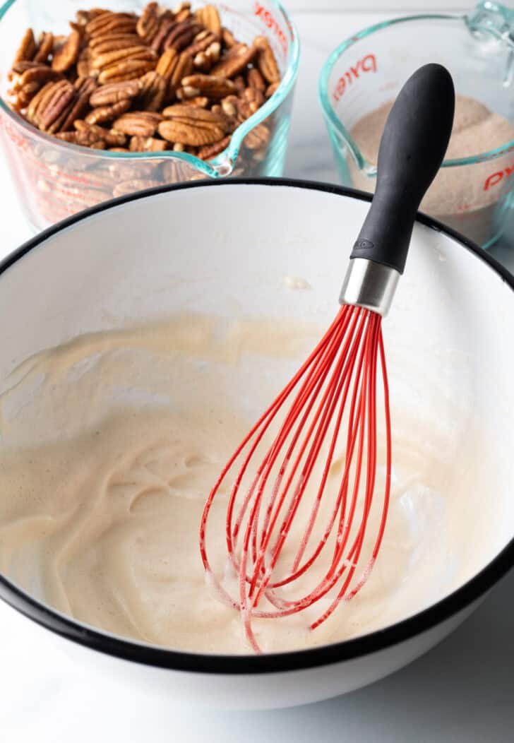 Whisking the candy coating with a red whisk in a large white bowl.