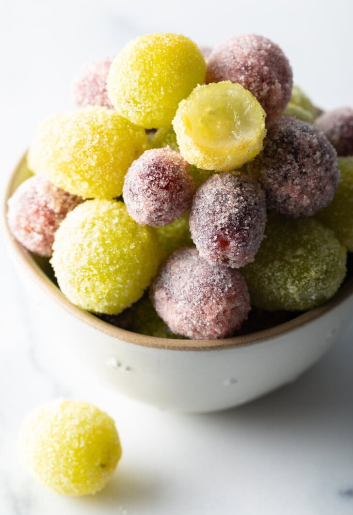 a bowl of green and purple candy grapes. One of the green grapes has been bitten in half to show the inside.