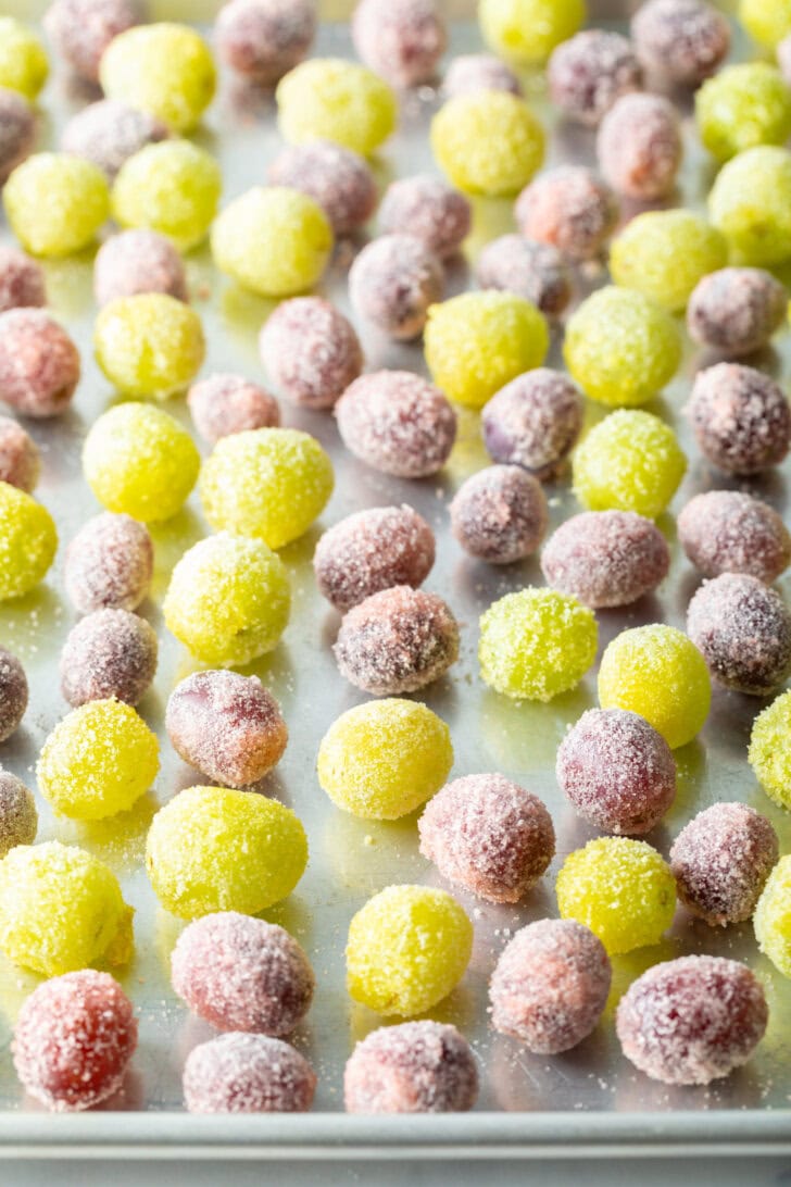 Top down view of a blend of green and purple grapes candy coated and spread on a baking sheet.