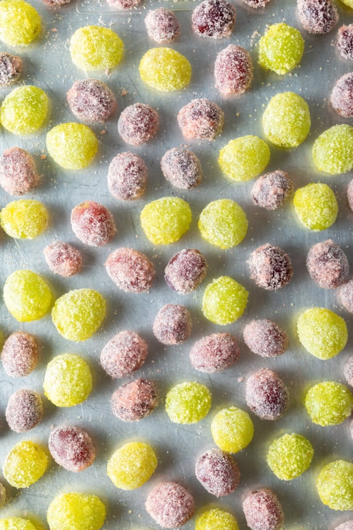 Top down view of a blend of green and purple grapes candy coated and spread on a baking sheet.