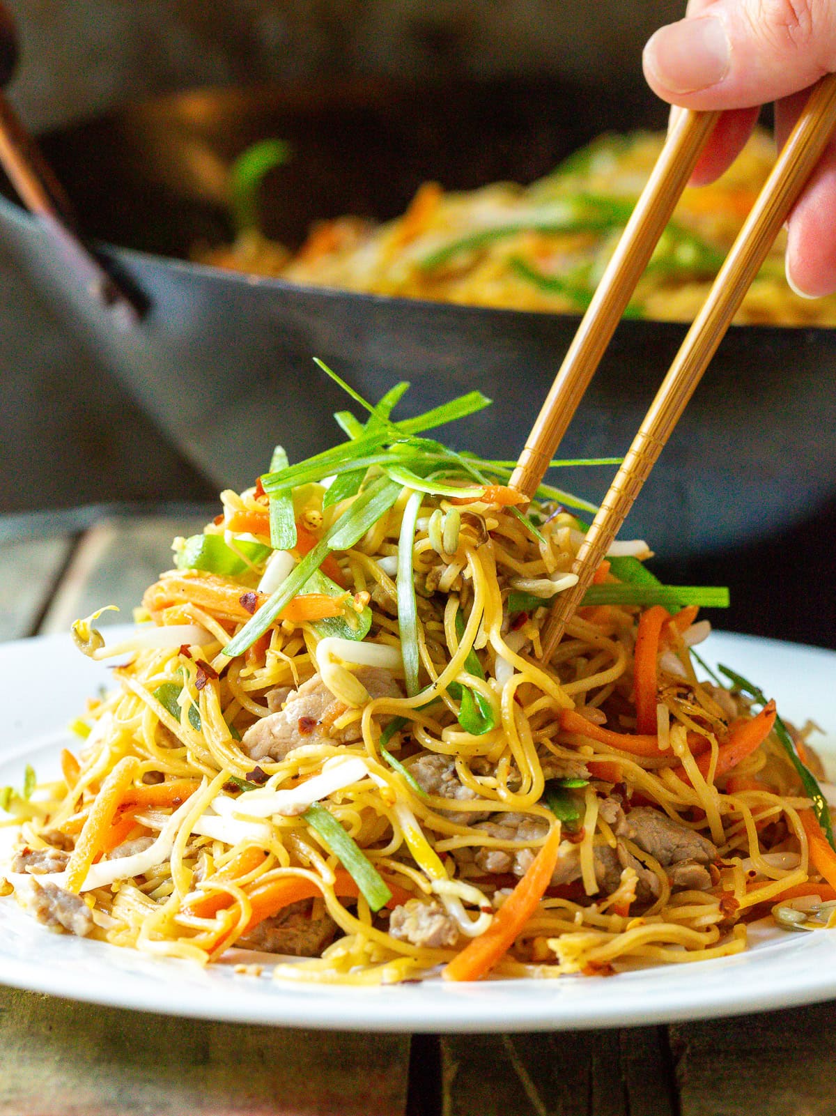 Chopsticks next to a large plate of cantonese noodles. 