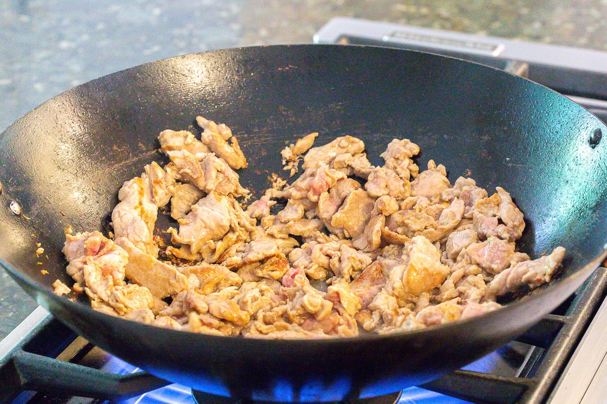 Searing the pork in a large wok for Cantonese Noodles