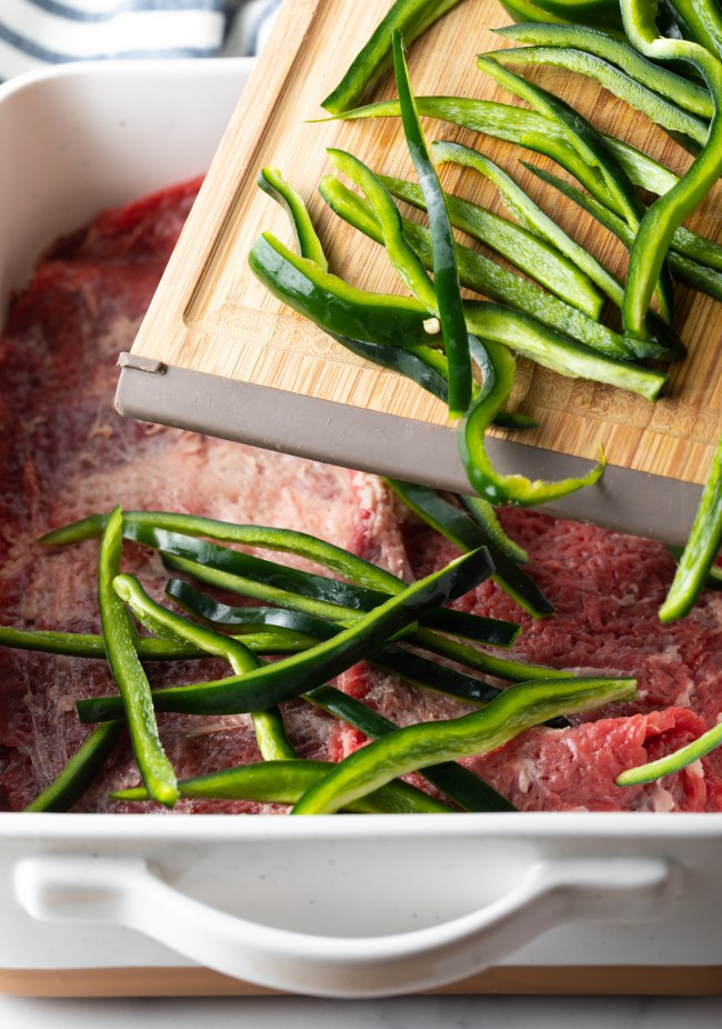 pepper strips being added to raw steak in a baking dish