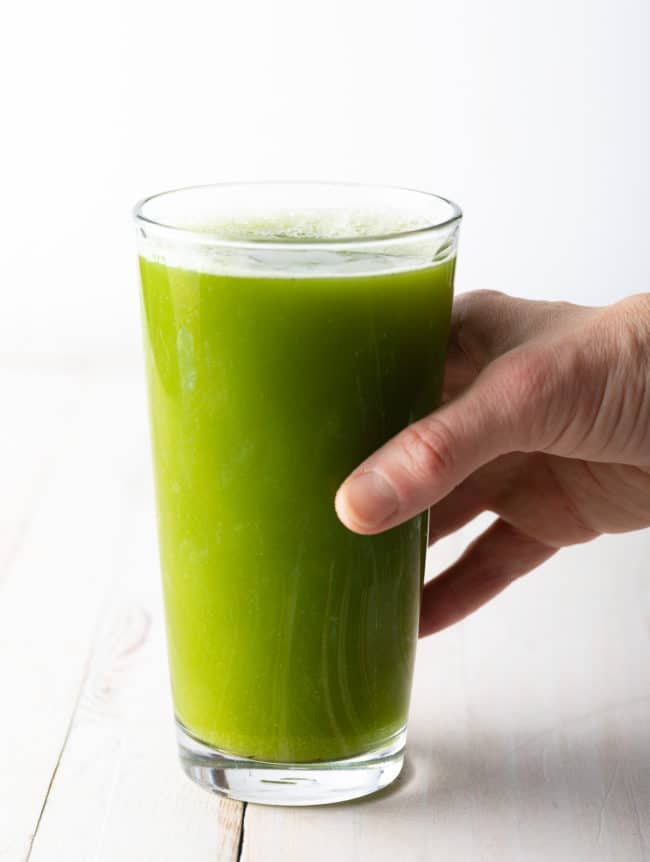 Hand holding a glass of celery juice. 